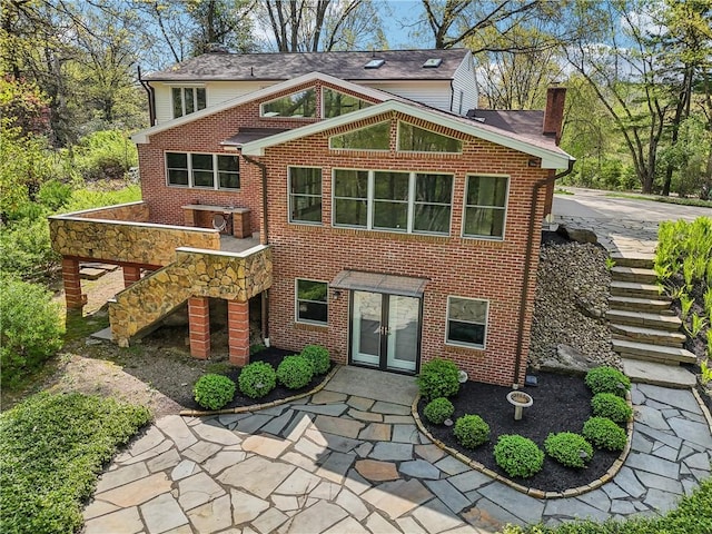 back of property with stairway, french doors, a chimney, and brick siding