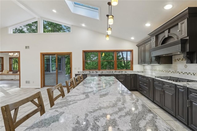 kitchen featuring stainless steel gas stovetop, a skylight, light stone counters, decorative backsplash, and hanging light fixtures
