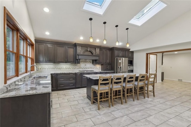 kitchen featuring a sink, appliances with stainless steel finishes, a skylight, decorative backsplash, and vaulted ceiling