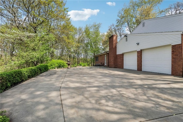 view of side of home with brick siding, driveway, a garage, and a chimney