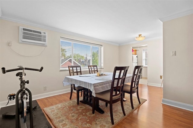 dining space featuring a wall mounted AC, crown molding, wood finished floors, and baseboards