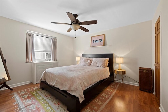 bedroom with radiator heating unit, baseboards, wood finished floors, ceiling fan, and cooling unit