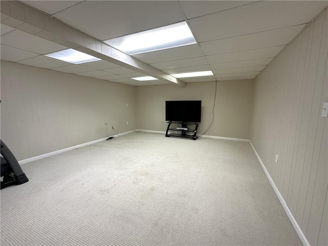 finished basement featuring a paneled ceiling, carpet floors, baseboards, and wooden walls