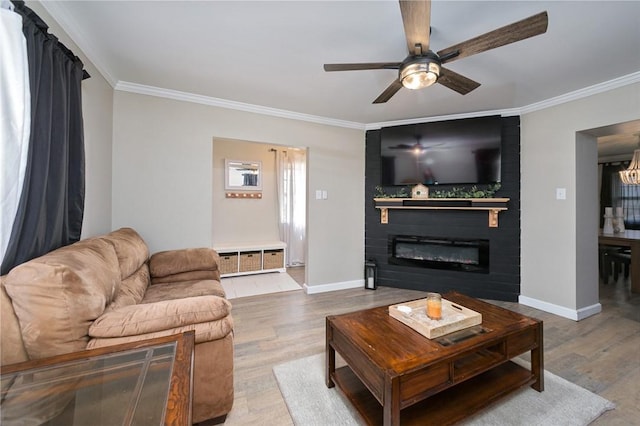 living area featuring wood finished floors, ornamental molding, a ceiling fan, baseboards, and a fireplace