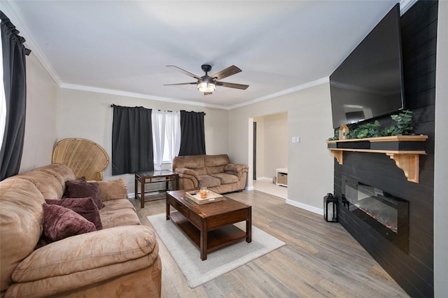 living room featuring ornamental molding, ceiling fan, light wood-style floors, a glass covered fireplace, and baseboards