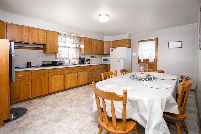 kitchen featuring white appliances, brown cabinetry, light countertops, a sink, and light floors