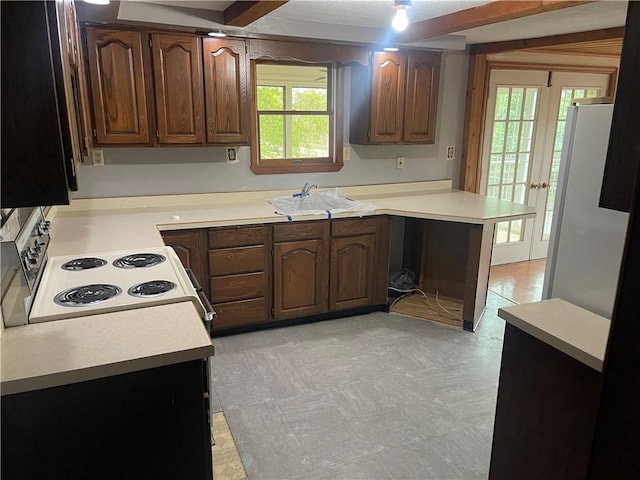 kitchen with a sink, electric range oven, freestanding refrigerator, light countertops, and a peninsula