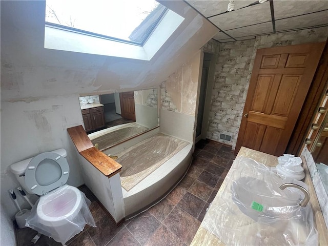 bathroom with a skylight, a garden tub, stone finish flooring, vanity, and toilet