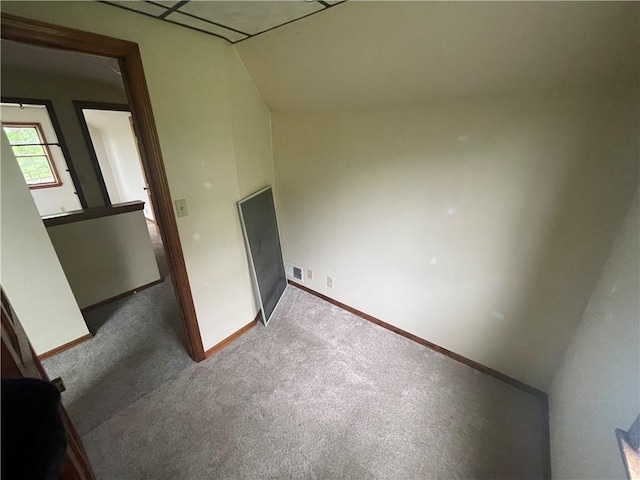carpeted empty room featuring baseboards and vaulted ceiling
