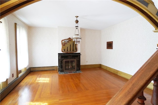 unfurnished living room with a chandelier, arched walkways, wood finished floors, a baseboard radiator, and a fireplace with flush hearth