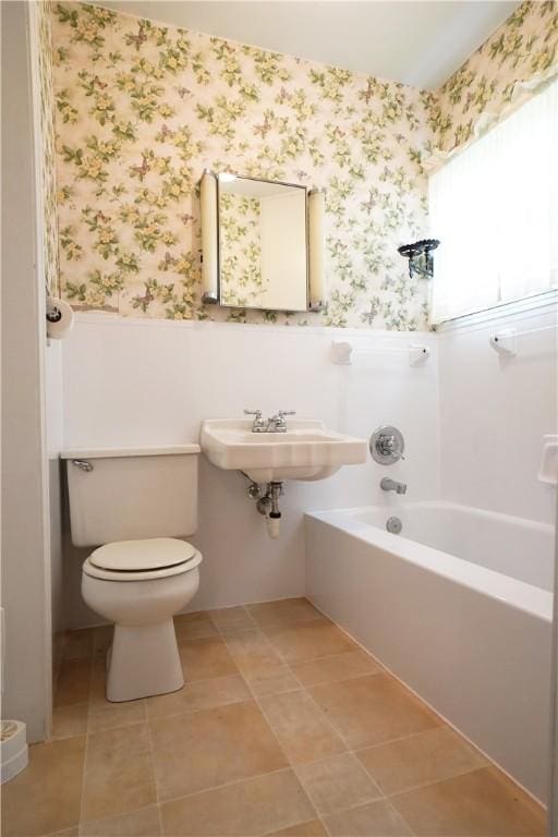 bathroom featuring wallpapered walls, wainscoting, toilet, a tub to relax in, and tile patterned floors