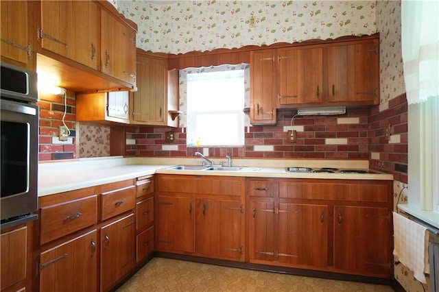 kitchen with wallpapered walls, stainless steel oven, light countertops, brown cabinetry, and a sink