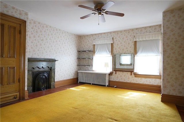 unfurnished living room featuring radiator, a ceiling fan, carpet flooring, wallpapered walls, and baseboards
