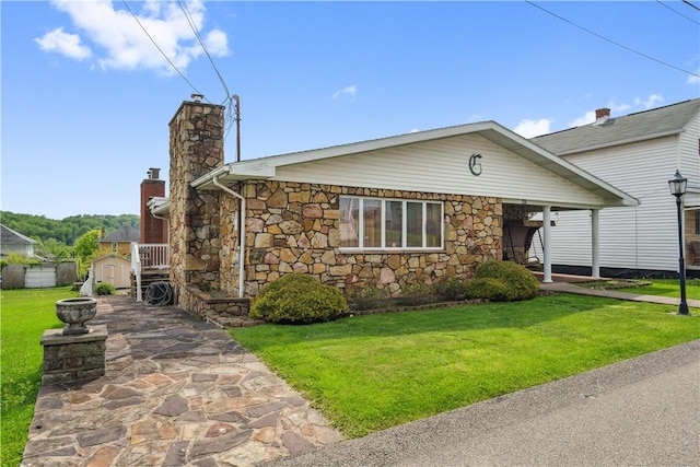 view of front of property with a chimney, a front lawn, stone siding, and a storage unit