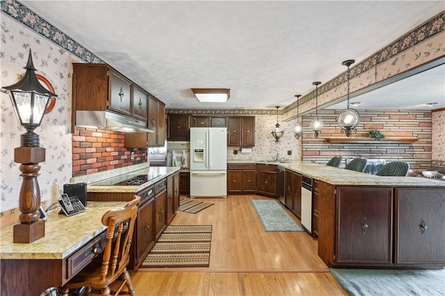 kitchen featuring white fridge with ice dispenser, wallpapered walls, under cabinet range hood, a peninsula, and light wood finished floors