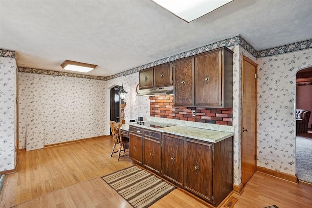 kitchen with wallpapered walls, arched walkways, under cabinet range hood, light wood-style flooring, and light countertops