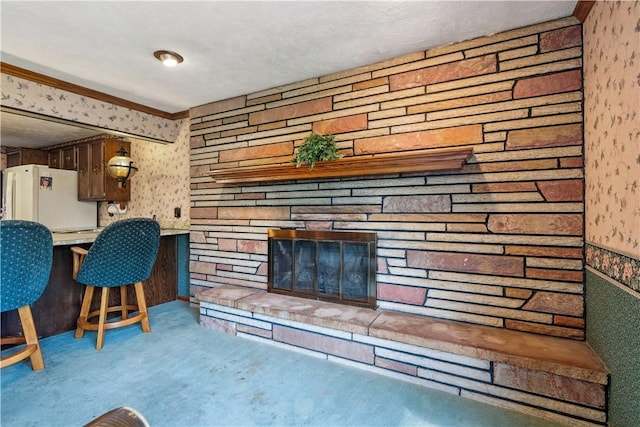 carpeted living area featuring wallpapered walls, a stone fireplace, and ornamental molding