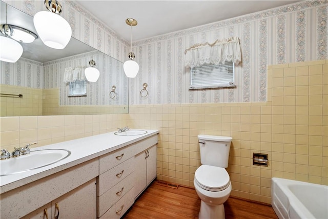 bathroom with wood finished floors, toilet, tile walls, wallpapered walls, and a tub to relax in
