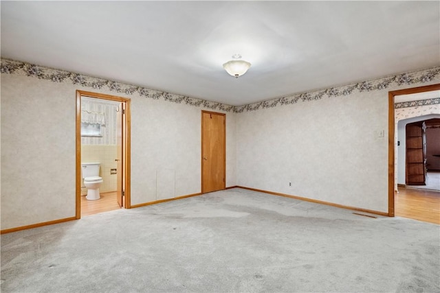 unfurnished bedroom with light carpet, baseboards, ensuite bath, and a closet