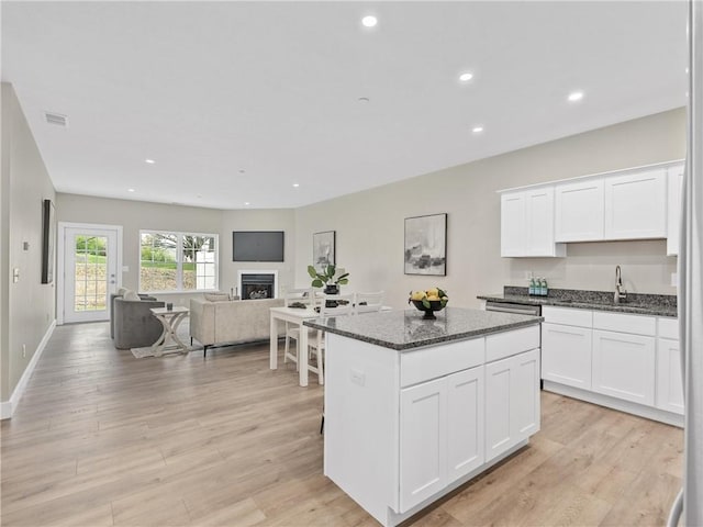 kitchen with a sink, a center island, recessed lighting, dark stone countertops, and white cabinets