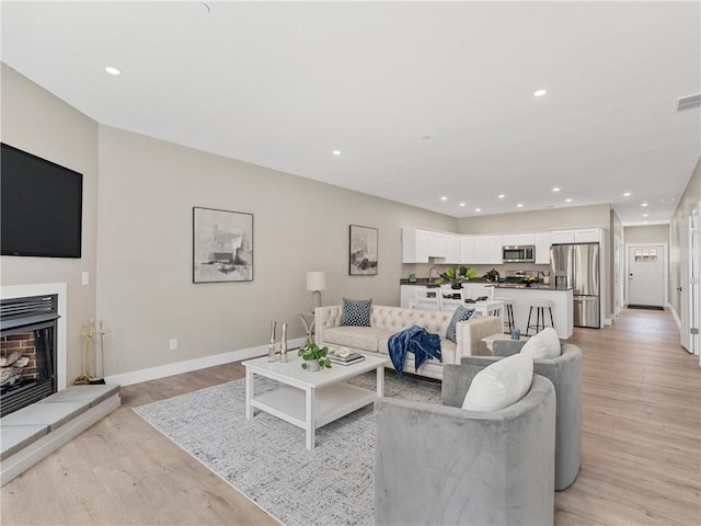 living room with baseboards, light wood-style floors, recessed lighting, and a fireplace with raised hearth