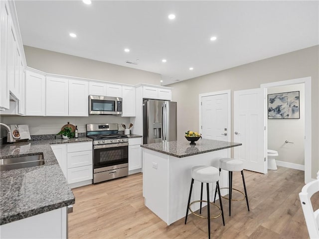 kitchen featuring appliances with stainless steel finishes, a sink, a kitchen island, a breakfast bar, and white cabinets