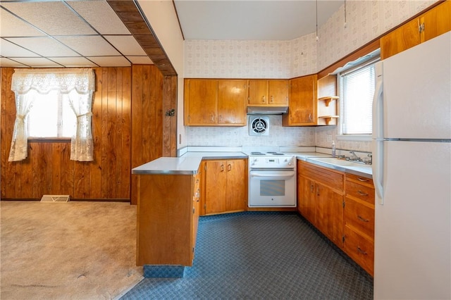kitchen with white appliances, a sink, brown cabinetry, a peninsula, and light countertops