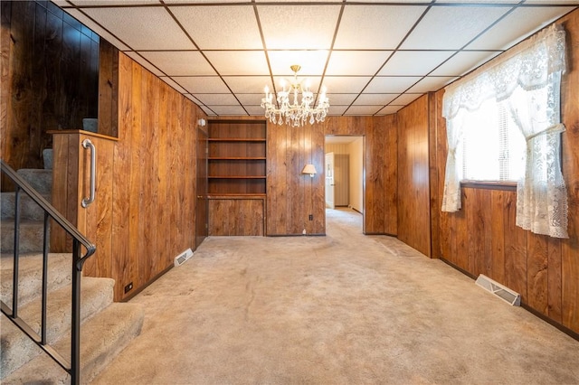 unfurnished living room with wood walls, stairs, a chandelier, carpet flooring, and built in features