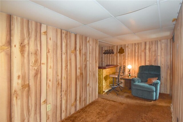 sitting room featuring wood walls, carpet floors, and a paneled ceiling
