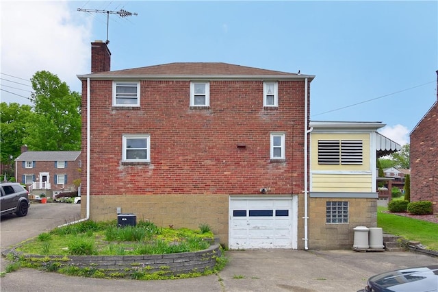 back of property featuring a chimney, an attached garage, brick siding, and driveway
