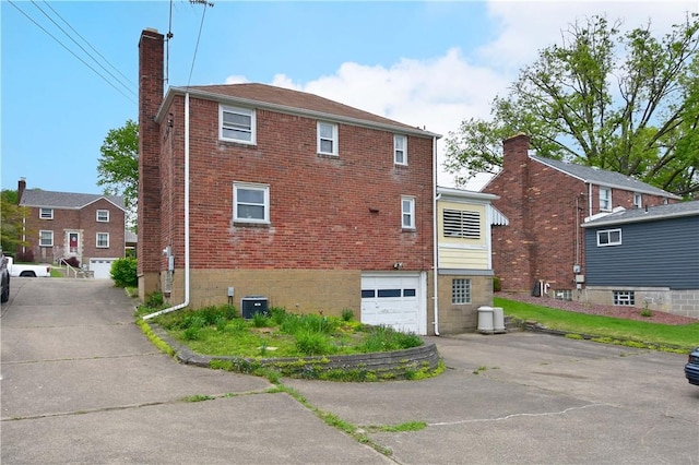 back of house featuring a chimney, driveway, a garage, and brick siding