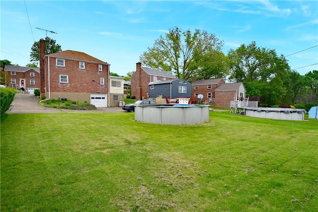 view of green lawn with a garage, a covered pool, and driveway