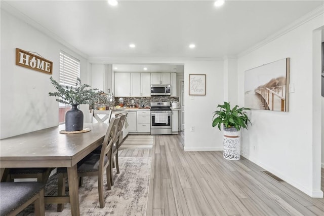 kitchen featuring appliances with stainless steel finishes, ornamental molding, white cabinetry, tasteful backsplash, and light wood-style flooring
