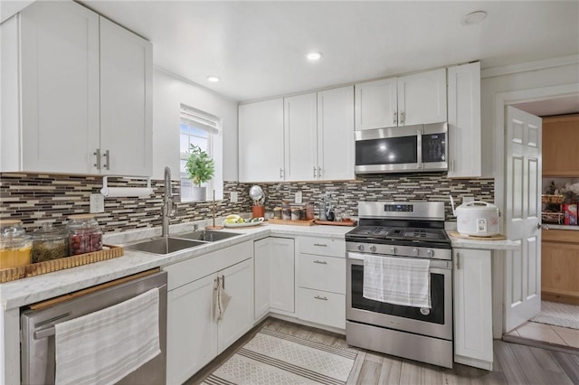 kitchen with appliances with stainless steel finishes, a sink, light wood-style flooring, white cabinets, and recessed lighting