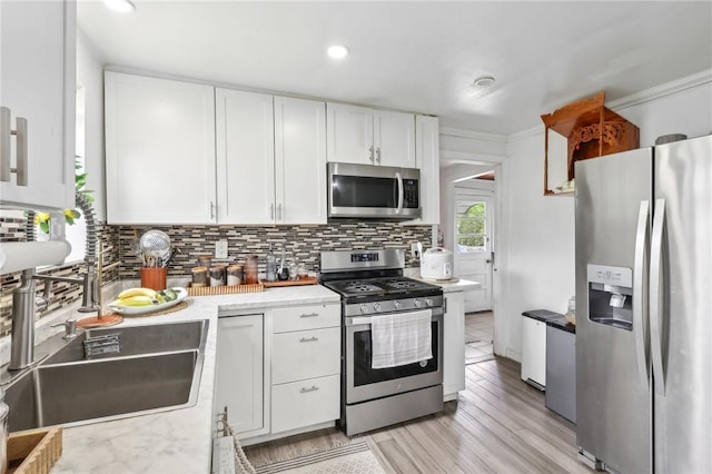 kitchen featuring appliances with stainless steel finishes, backsplash, white cabinetry, light countertops, and ornamental molding