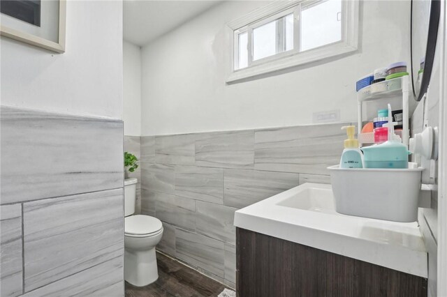 half bathroom with tile walls, toilet, vanity, a wainscoted wall, and wood finished floors