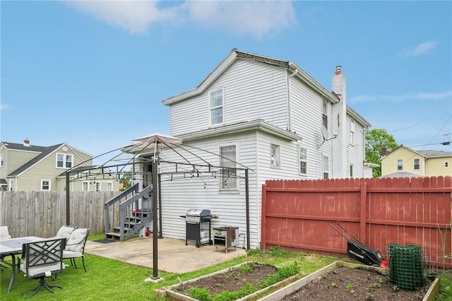 back of house featuring a vegetable garden, a patio area, a chimney, and stairway