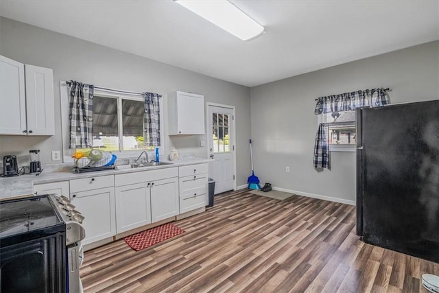 kitchen with a sink, stainless steel range with electric stovetop, light wood finished floors, light countertops, and white cabinets