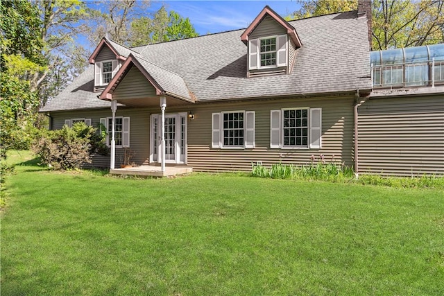 back of property featuring a chimney, a lawn, and roof with shingles