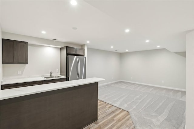 kitchen with freestanding refrigerator, a sink, recessed lighting, light countertops, and dark brown cabinetry