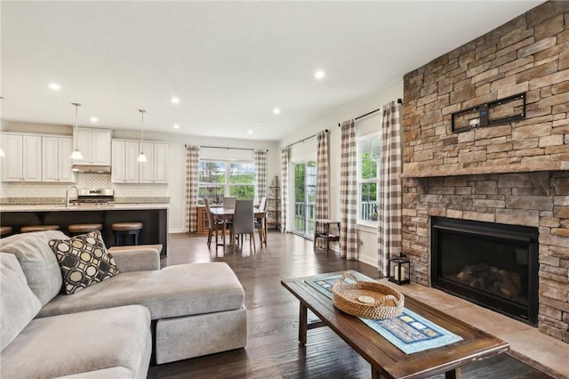 living room with recessed lighting, baseboards, a stone fireplace, and dark wood-style floors