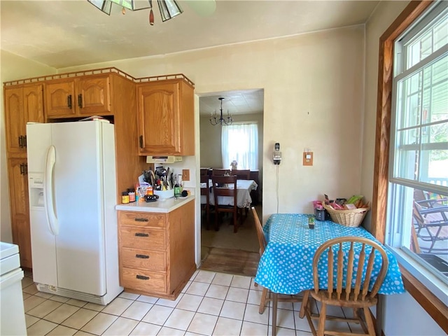 kitchen with white fridge with ice dispenser, light countertops, light tile patterned flooring, a chandelier, and brown cabinets