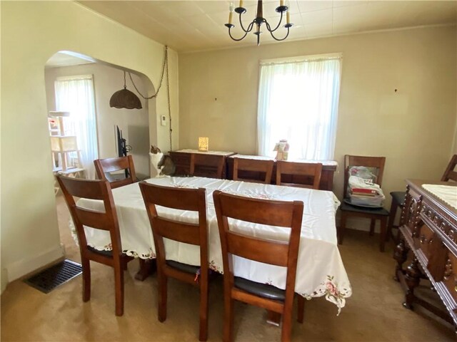 carpeted dining room featuring arched walkways and a chandelier