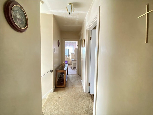 hallway featuring light colored carpet and baseboards
