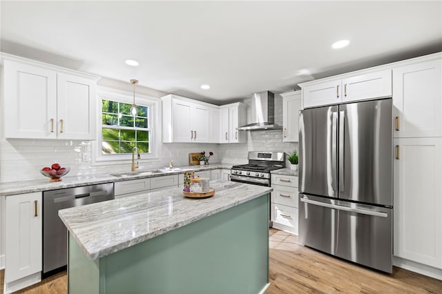 kitchen with appliances with stainless steel finishes, wall chimney range hood, a sink, white cabinetry, and recessed lighting