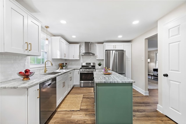 kitchen with appliances with stainless steel finishes, a sink, wall chimney range hood, a kitchen island, and white cabinets