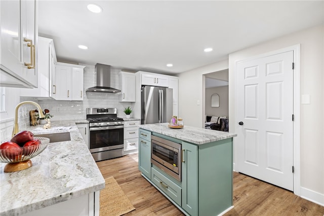 kitchen featuring appliances with stainless steel finishes, wall chimney exhaust hood, green cabinets, a sink, and white cabinetry