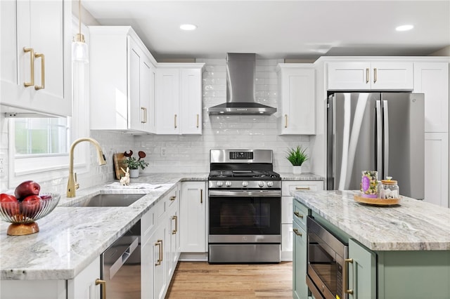 kitchen with stainless steel appliances, wall chimney range hood, a sink, white cabinets, and recessed lighting