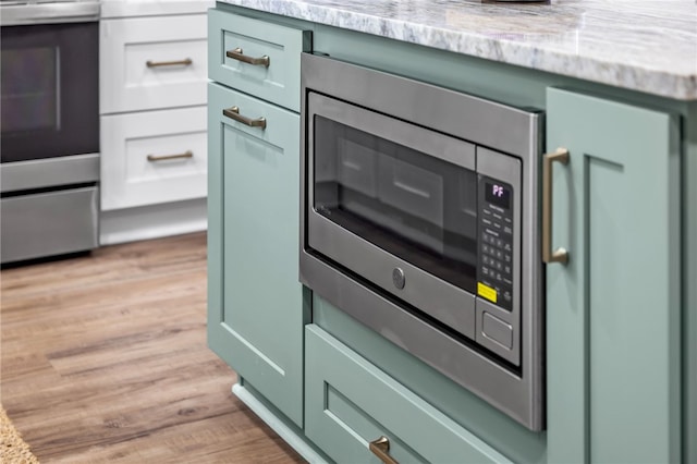 kitchen view of green cabinets, stainless steel appliances, light wood-style floors, and light stone countertops