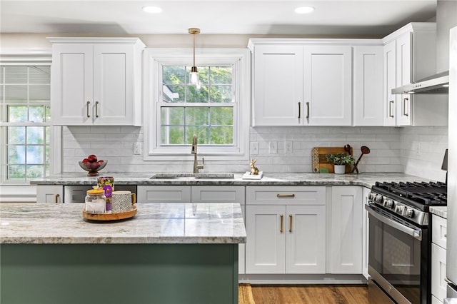 kitchen with stainless steel range with gas cooktop, a sink, wall chimney range hood, white cabinetry, and light stone countertops